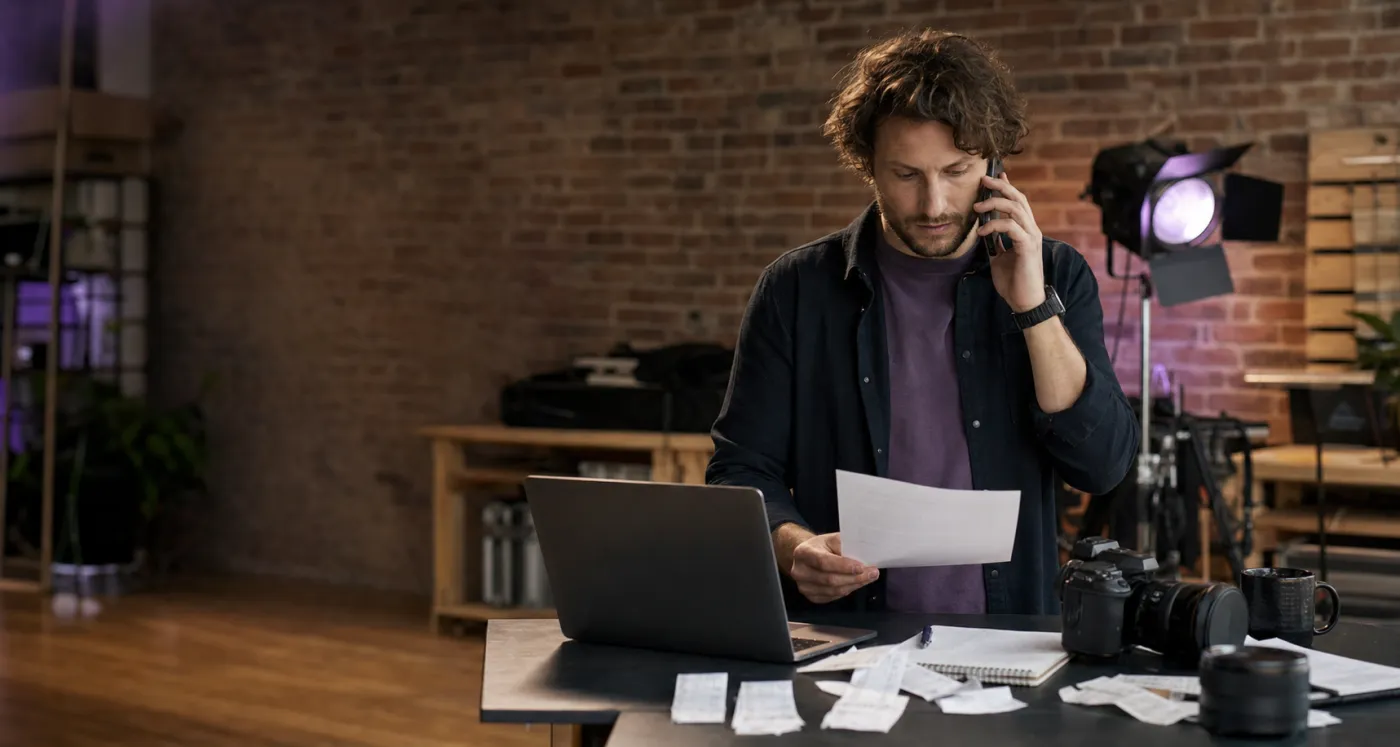 Freelance photographer on the phone sorting receipts and invoices for contractor tax deductions